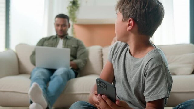 Gadget addicted family with devices at home multiracial mom and dad using laptops addict work ignoring sad child little boy son bored kid with phone smartphone on floor lack parents attention custody