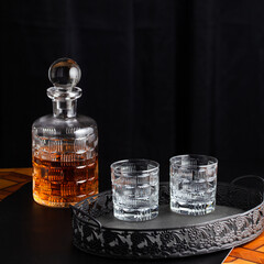 Whiskey bottle and goblets on a wooden table and black tray
