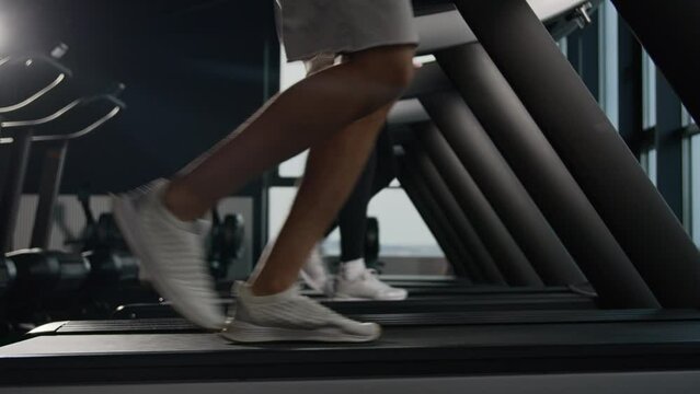 Close up male legs in sport shoes running on treadmill run jog in fitness club unrecognizable couple runners woman and man feet jogging in sports gym stride move step cardio exercising on racetrack