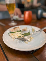 Lunch and Cocktails at an Outdoor Cafe. Sitting at a wooden table enjoying a fresh lunch in France. A fork rests on a white plate signaling the person is replete. Beer and cocktails rest on the table.