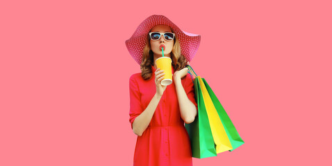 Portrait of beautiful young woman model with colorful shopping bags drinking juice in summer hat