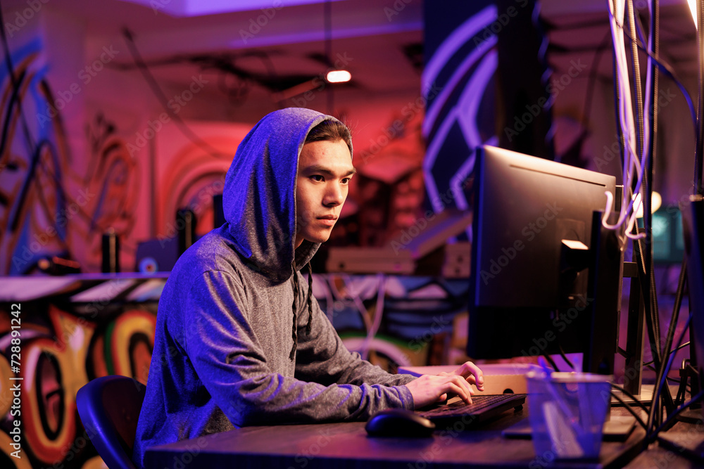 Poster asian internet scammer cracking password on computer to get access to database. young man in hood wr
