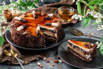 Chocolate cake with caramel, condensed milk, cream and walnuts on dark background with spring...