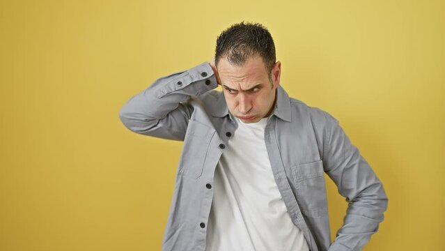 Young hispanic man, perplexed, wearing a shirt, stands in doubt against a yellow background, lost in a pensive question