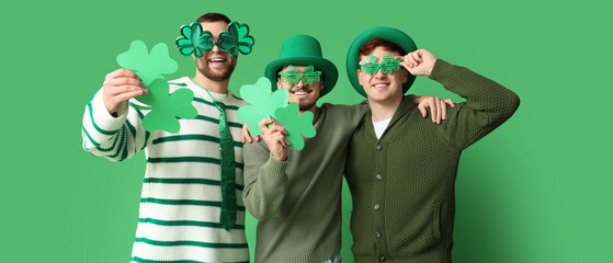 Happy young men with clovers on green background. St. Patrick's Day celebration