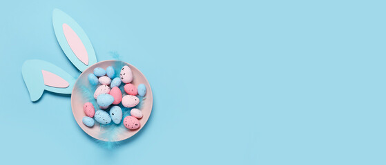 Plate of Easter eggs, feathers and bunny ears on light blue background with space for text