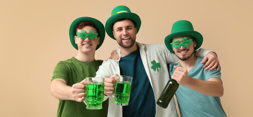 Happy young men in leprechaun's hats and with green beer on beige background. St. Patrick's Day...