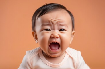 Close-up on small Asian boy toddler crying loudly against beige backdrop in need for baby care