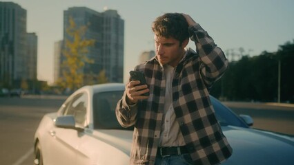 Caucasian confused man disappointed 30s guy millennial male businessman worried stressed car driver near luxurious modern auto on city parking outdoors reading bad news mobile phone problem loss upset