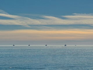 Santa Barbara, CA, USA - January 28, 2024: Five offshore oil rigs on horizon in Pacific Ocean under morning blue sky cover with orange sunlight. Swimmer in front 