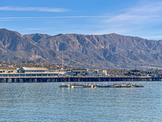 Santa Barbara, CA, USA - January 28, 2024: Pelican flock on artificial floating device in front of Stearn Wharf. Mountain range in back under blue cloudscape