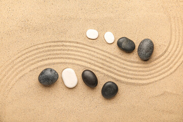 Fototapeta na wymiar Black and white spa stones on sand with lines. Zen concept
