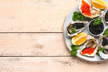 Plate of tasty oysters with lemon, black and red caviar on light wooden background