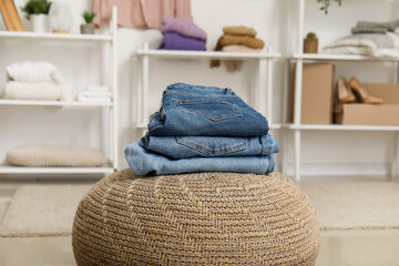 Stack of stylish jeans on wicker ottoman in wardrobe at home