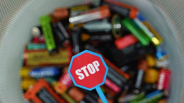 A person throws batteries into a bin. Stop pollution by batteries. Different battery and stop sign rotate in a bin
