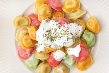 Plate of boiled colorful dumplings with sour cream and dill, closeup