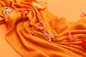 Autumn composition with knitted scarf, sunglasses and leaf on orange background