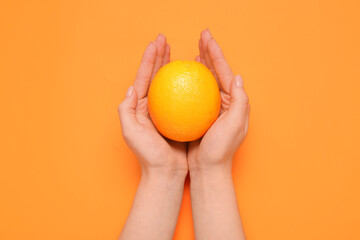 Female hands holding fresh orange on color background
