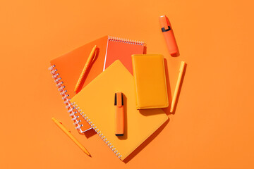 Pens, markers and notebooks on orange background