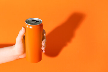 Female hand holding soda can on orange background