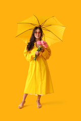 Beautiful young Asian woman with umbrella and bouquet of pink dahlias on yellow background
