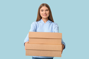 Pretty young woman with cardboard boxes on blue background. Moving house concept