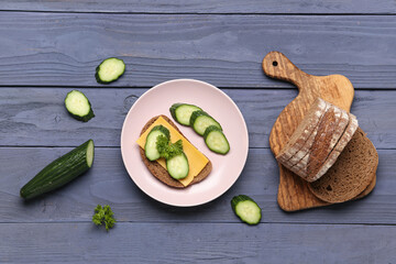 Tasty sandwich with cheese and cucumber in plate on grey wooden background