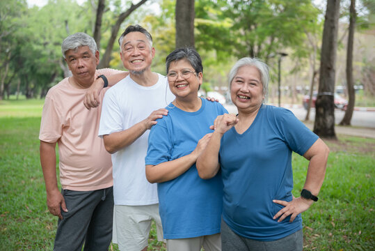 Asian elderly men and women Standing for photographers to take photos in the park before playing sports and exercising. Smile happily in retirement, take care of your health.