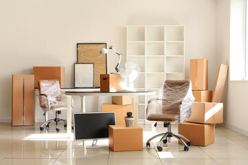 Interior of light office with chair wrapped in stretch film and cardboard boxes on moving day