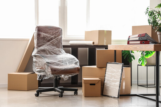 Interior of light office with chair wrapped in stretch film and cardboard boxes on moving day