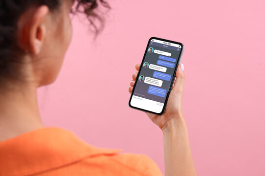 Woman texting with friend using messaging application on smartphone against pink background, closeup