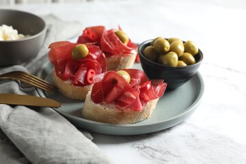 Delicious sandwiches with bresaola, cream cheese and olives served on white marble table, closeup
