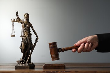 Judge striking mallet at wooden table against grey background, closeup. Figure of Lady Justice...