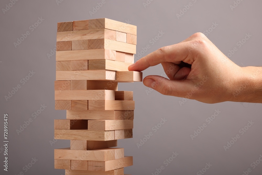 Poster Playing Jenga. Man removing wooden block from tower on grey background, closeup