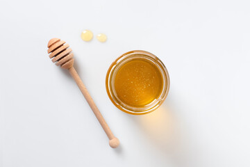 Tasty honey in glass jar and dipper on white background, top view