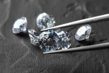 Tweezers with beautiful shiny diamond above dark gray table, closeup