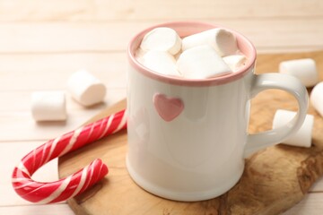 Tasty hot chocolate with marshmallows and candy cane on light wooden table, closeup