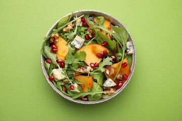 Tasty salad with persimmon, blue cheese, pomegranate and walnuts served on light green background,...