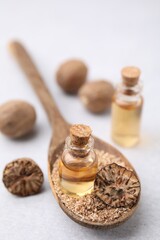 Nutmeg essential oil and spoon with ground nuts on light table, closeup