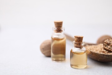 Nutmeg essential oil and spoon with ground nuts on light table, closeup. Space for text
