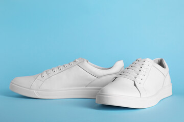 Pair of stylish white sneakers on light blue background
