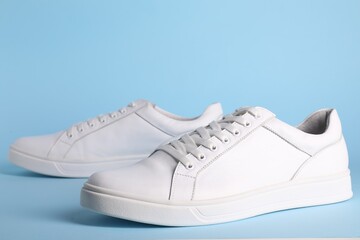 Pair of stylish white sneakers on light blue background