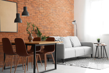 Interior of modern living room with cozy grey sofa and dining table near brown brick wall