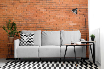 Interior of modern living room with cozy grey sofa and coffee table near brown brick wall
