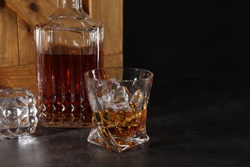 Whiskey in glass and bottle near wooden crate on dark table against black background. Space for text