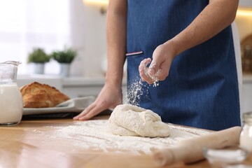 Making bread. Man sprinkling flour onto dough at wooden table in kitchen, closeup