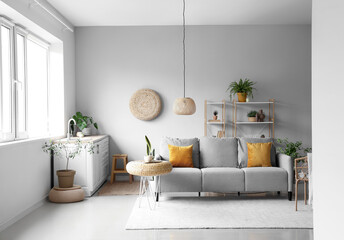 Interior of light living room with cozy grey sofa, houseplants and wicker poufs