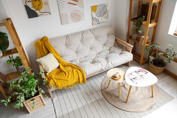 Interior of light living room with cozy white sofa, coffee table and houseplants