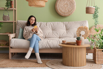 Pretty young woman with mobile phone resting on cozy white sofa in living room