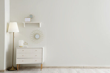 Chest of drawers with lamp, mirror and decor near white wall